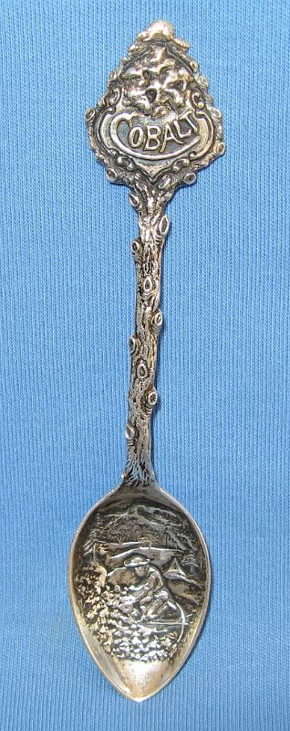 Cobalt Ontario Canada.JPG - SOUVENIR MINING SPOON COBALT ONTARIO CANADA, CANADA'S SILVER CAPITAL - Sterling demitasse spoon with embossed miner, pick and ore scene in bowl, with figural twig branch handle and ornate top, marked on top COBALT for Cobalt, Ontario, Canada’s silver capital, reverse marked Sterling, 4 1/4 in. long  [Cobalt, Ontario, was the silver capital of Canada and the birthplace of Canadian hard rock mining.  It played an important role in the evolution of the mining and financial industries in Canada. Located about six hours drive (250 miles) due north of Toronto, silver was discovered in the Cobalt area in the summer of 1903 during construction of the Temiskaming and Northern Ontario Railway from North Bay to the small farming communities of Haileybury and New Liskeard on the shores of Lake Temiskaming. The initial discovery of silver occurred at a point 103 miles from North Bay at what is now Cobalt.  The town of Cobalt was incorporated in 1906 and soon became a boom town when its population swelled and peaked at 10,000 in 1909. The district became one of the largest silver-producing areas in the world, eventually yielding a total of 460 million ounces of silver. That’s almost $16-billion worth at today’s silver prices. The peak year was 1911 when 34 mines produced about 30-million ounces of silver.  By the late 1920s the boom was winding down and Cobalt started to decline. Mining was revived in the 1950s then slowly dropped off, so that there are no active mines now. However, one mill still operates and there is exploration in the area.  The Cobalt silver boom has left a rich legacy of old buildings and mining structures, leading to its recognition by TV Ontario as Ontario’s Most Historic Town and designation as a Parks Canada National Historic Site.]